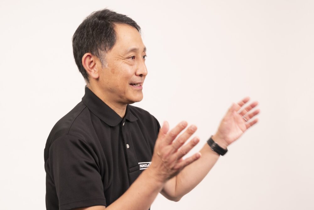 白い背景の前で、両手を広げて話す芥田さん